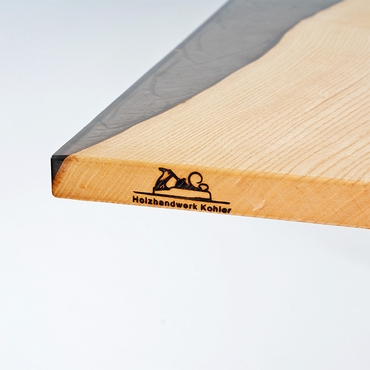 Ein Holztisch mit schwarzem Epoxidharz und dem eingebrannten Logo von Holzhandwerk Kohler.